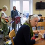 Jordan Wallace, left, tunes her mandolin as Barbara Steinhaus, right speaks with her colleagues before the start of the Bluegrass and Books event in the Tea Room on Brenau's Gainesville campus.