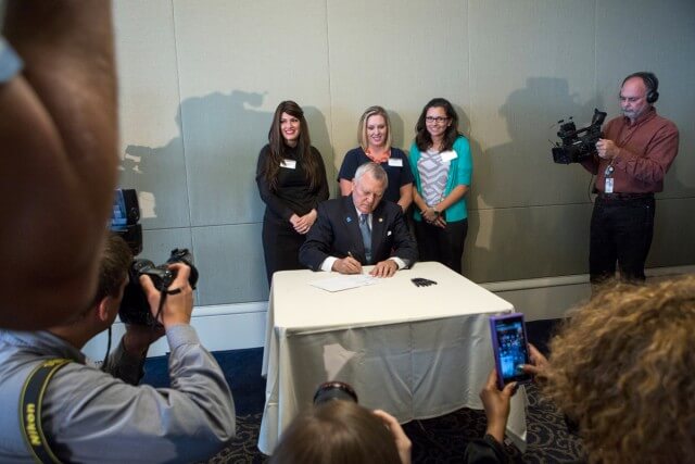 Governor Nathan Deal signs House Bill 62 into law during the Atlanta Press Club lunch Wednesday, April 29, in font of Brenau occupational therapy alumnae Rachel Strazynski, Shelby Wrenn and Allison Guisasola. HB 62, which helps special needs children of military personnel by lifting a one-year residency requirement before students can receive benefits, started as a class project the Brenau students worked on and pitched to Representative Kevin Tanner as they earned their graduate degrees.