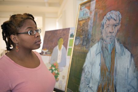 Dimond Leslie, a senior studio art major, looks at the paintings "Man at a Table" by Robert LaHotan, left, and "Self Portrait" by John Heliker, right, on display on April 13, 2016. (AJ Reynolds/Brenau/University)
