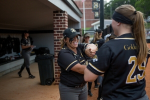 Brenau's Kelsey Payne, center, and Jessica Rathje laugh inside the team's dugout. (AJ Reynolds/Brenau University)