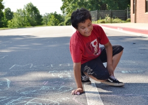Carlos Payero laughs while he uses sidewalk chalk to draw his favorite memories from his time in the RISE Summer Program. RISE is a collaborative six-week summer program created by community partners that reduces summer learning loss among low-income children through interactive programming.