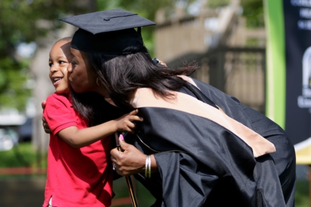 Aquarium Williams in graduation regalia kisses child on the cheek