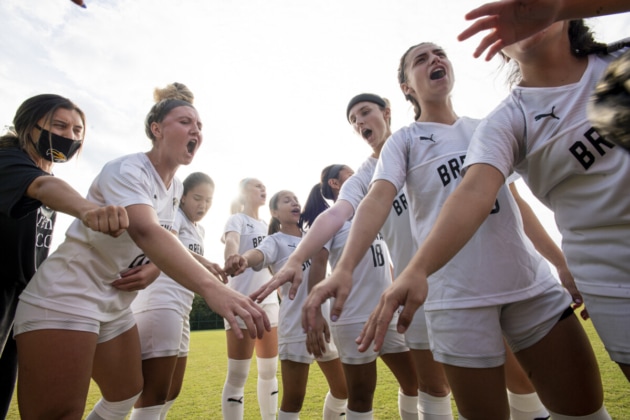 Female soccer players in a circle, each with one hand in the center.