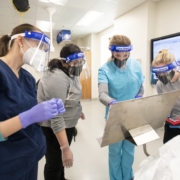 Physician Assistants in masks and face shields gather around display