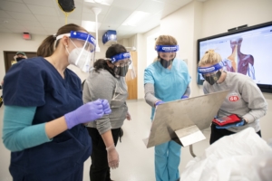 Physician Assistants in masks and face shields gather around display